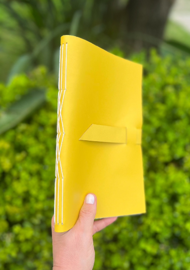 Caderno amarelo visto de lado, com costura branca aparente na lombada